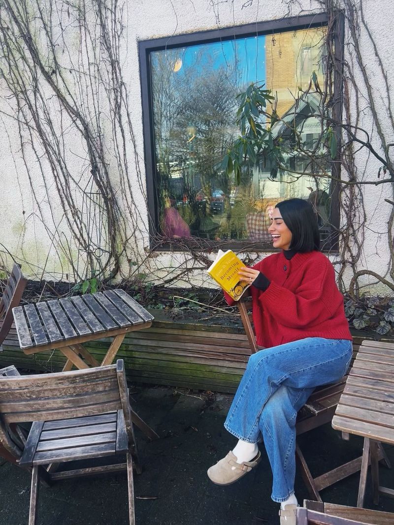 Bita laughing on a garden bench in a red sweater, reading Irvin Yalom's Becoming Myself