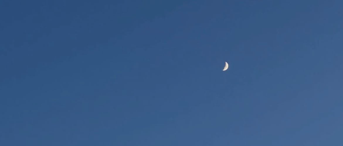A thin crescent moon in a clear blue evening sky